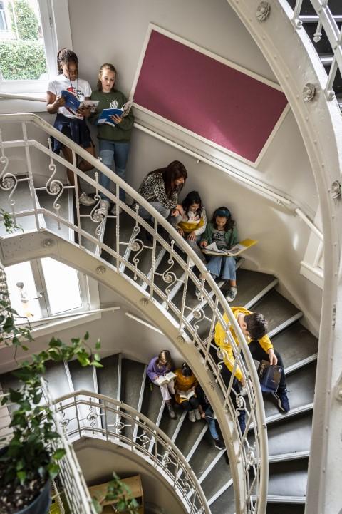 Kinderen lezen boeken in trappenhal van De Kleine Stad.